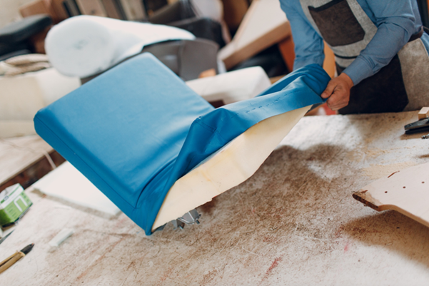 A craftsman is upholstering a sofa with new fabric