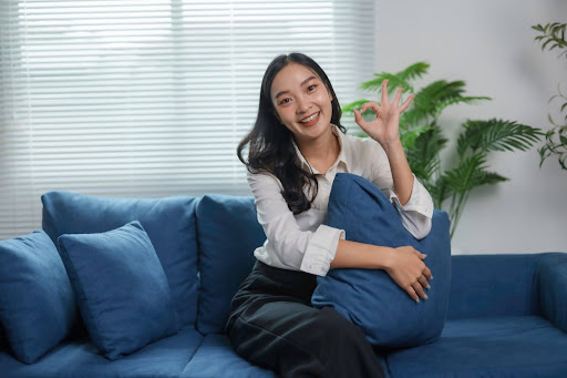 A woman sitting while embracing a plush blue cushion on a newly reupholstered blue sofa