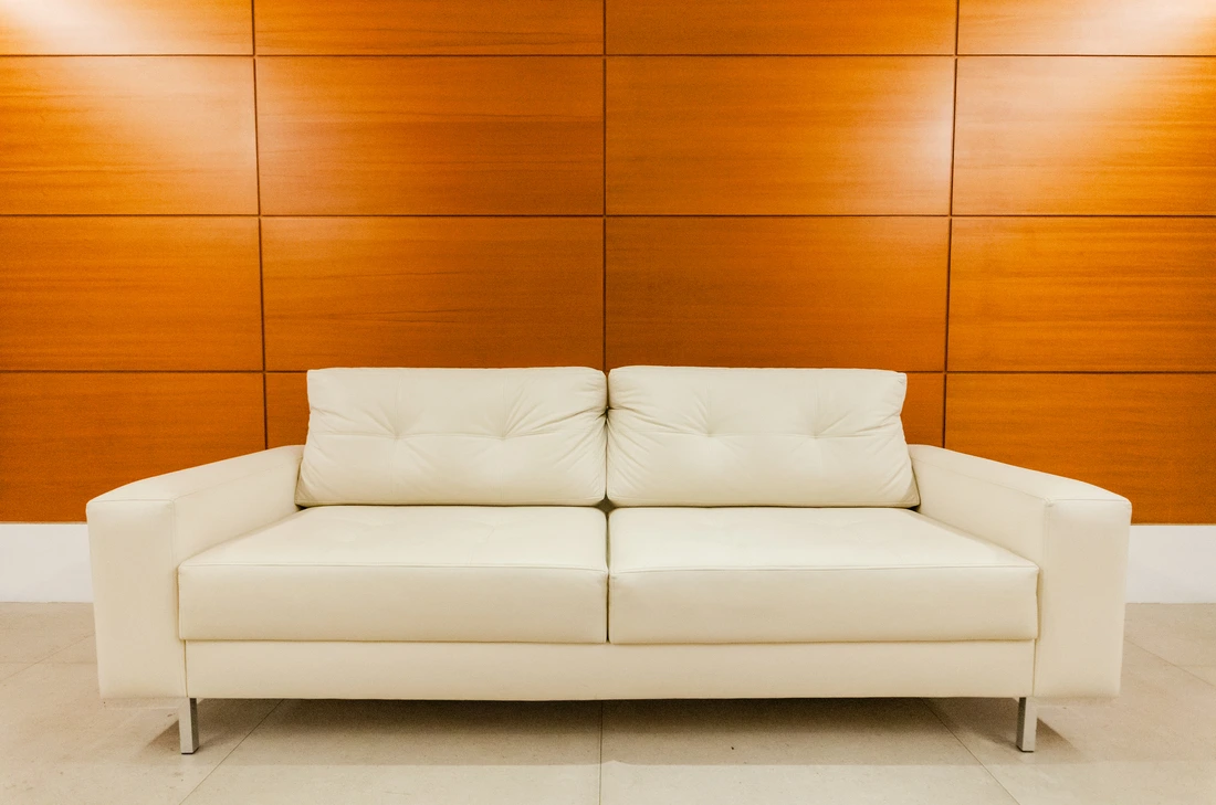 A sleek white leather sofa against a wooden wall in a modern living room