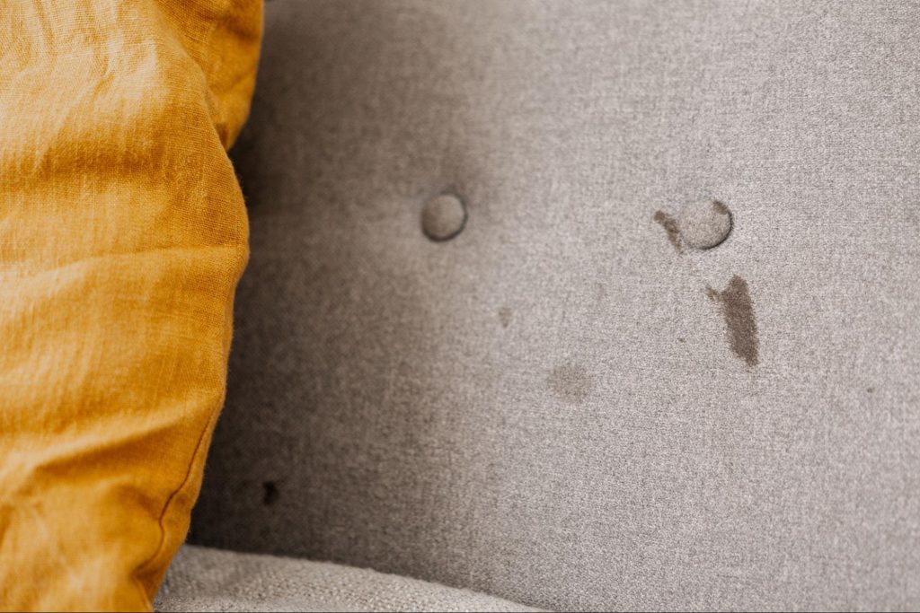 Dirty, stained, and fading textile on a sofa, indicating the need for deep cleaning or professional reupholstery.