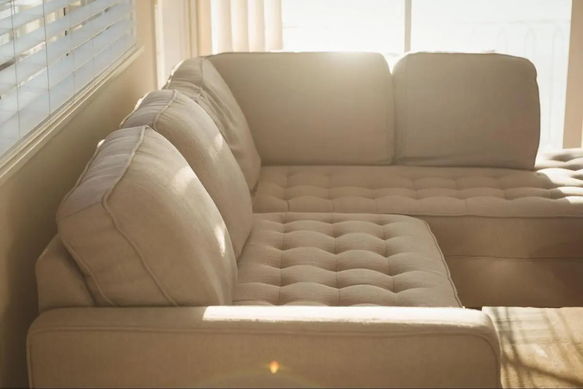 Grey tufted sectional sofa near a window, showing button tufting detail that increases upholstery cost